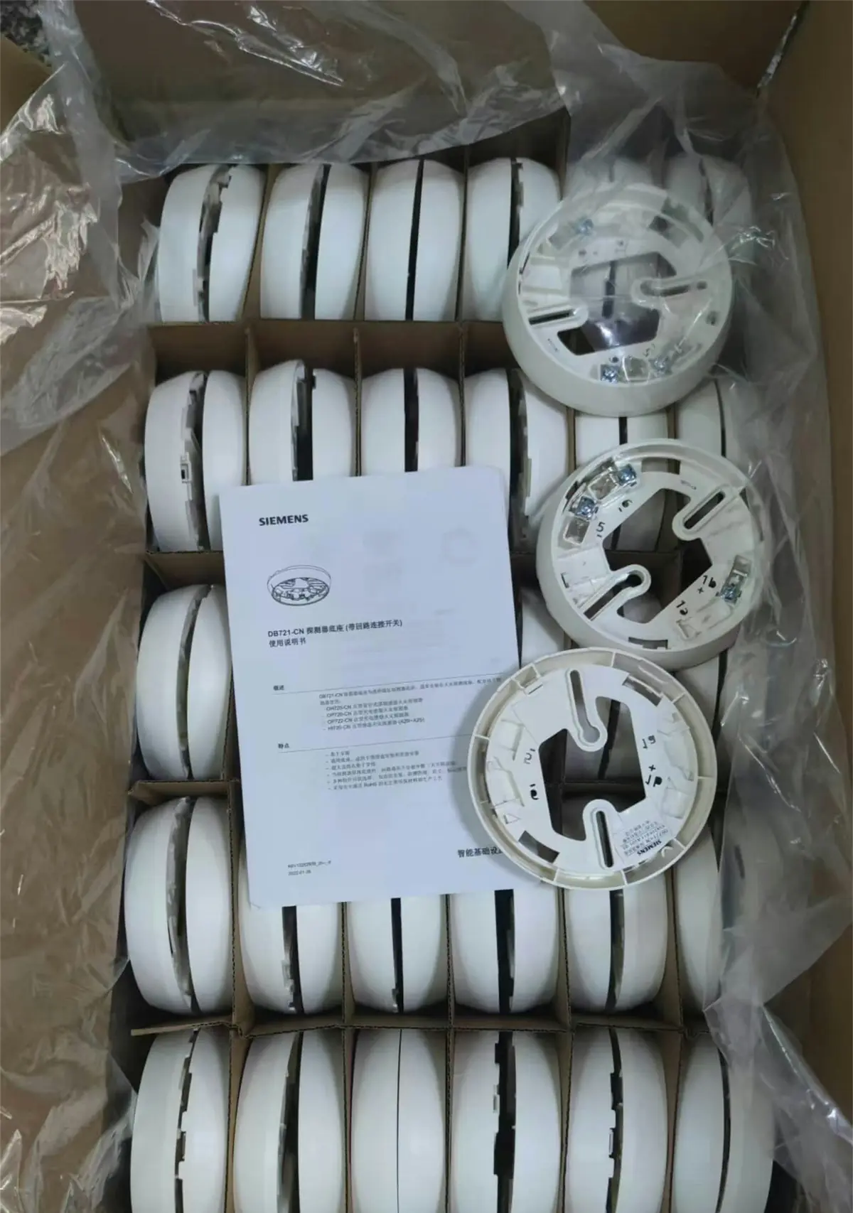 A carton of new white smoke alarms with their mounting bases and an instruction sheet.